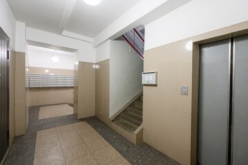 indoor hallway with beige tile walls, a staircase, mailbox area, and an elevator. The lighting is bright and artificial