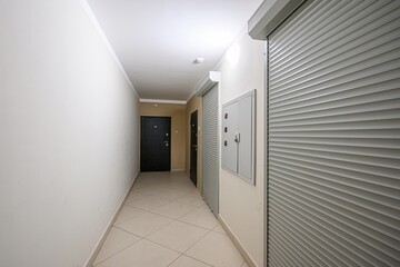 hallway features doors, roller shutters, and a utility box. The space is lit by a ceiling light, highlighting the tiled floor