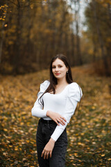 Girl in jeans and a white sweater in the forest in autumn, fallen leaves of trees are visible in...
