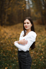 Girl in jeans and a white sweater in the forest in autumn, fallen leaves of trees are visible in...