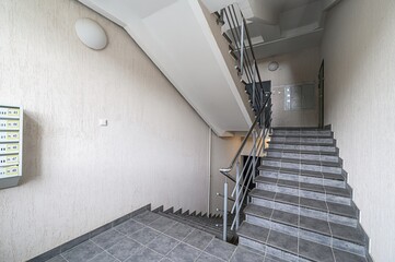 Interior shot of a stairwell with gray tiled stairs and walls. Mailboxes are visible on the wall