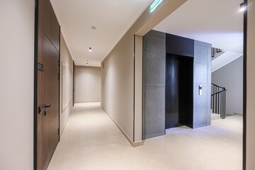 interior shot of a hallway featuring apartment doors, an elevator, and a staircase. The color...