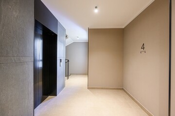 modern hallway with a black elevator, neutral walls, and beige tiles. A sign with the number 