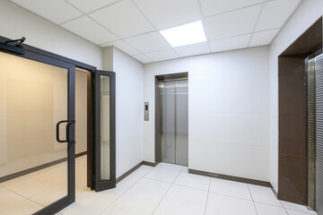clean, modern interior space featuring white tiled walls and floor. An elevator and an open glass...