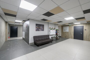 Modern lobby with tiled floors, a sofa, and a varied ceiling tile pattern. Two dark doors are visible