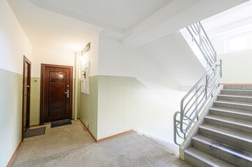 Interior shot of a building entrance: doors, walls painted in two-tone green and white, and stairs with metal railings leading upwards