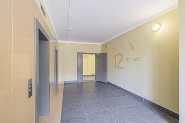 Interior shot of an apartment building hallway featuring elevators on one side and apartment number markings on the wall