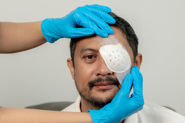 A young man undergoing eye treatment with bandage and eye patch, representing injury care, healing,...
