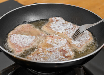 Thin pork chops dusted with flour, fried in hot oil in a pan