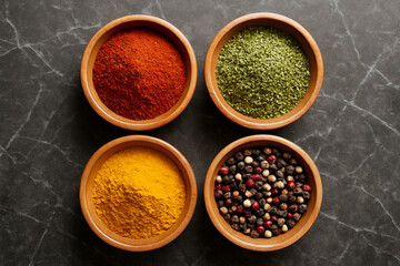 Assortment of colorful spices in wooden bowls on a dark stone surface