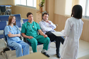 Obraz premium Female Doctor explaining treatment details to seated medical team, sharing ideas and reviewing patient files together in hospital meeting room.