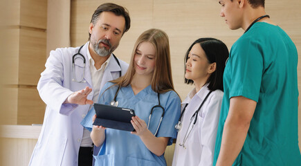 Mature male doctor sharing patient information with medical team on digital tablet in hospital,...