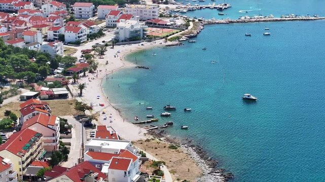Drone captures Mali Dubrovnik beach and adjacent marina in Povljana with boats, turquoise water and stone shores under the bright summer sun