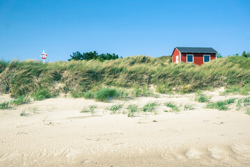 Kleines rotes Holzhäuschen rechts im Bild in einer Düne stehend, horizontal