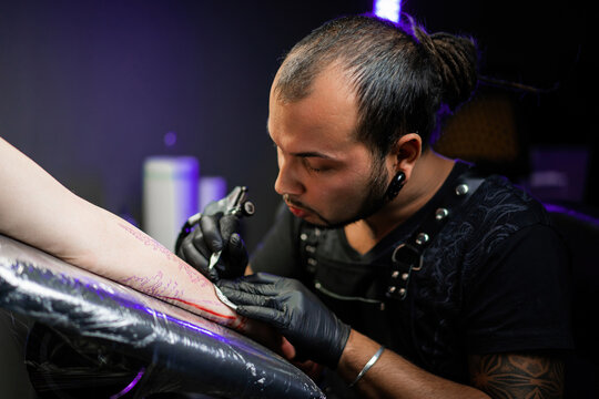Man tattoo master with dreadlocks showing process creation tattoo, female body - Powered by Adobe