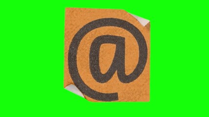 Black at symbol printed on orange paper with curled edges, placed on a vibrant green background for a bold contrast.