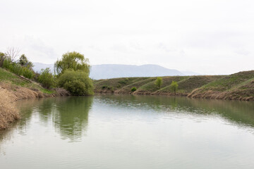 Obraz premium Calm river surrounded by grassy hills