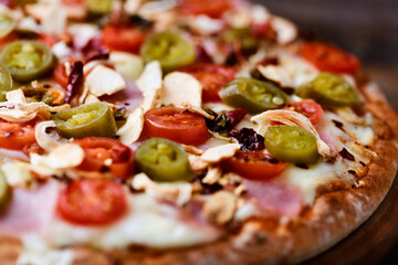 Pizza with ham, cherry tomatoes and mozzarella cheese. Wooden background. Soft focus. Close up.	