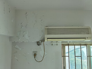 a close up photo on an air conditioner on the wall above the window, with several painting cracks...