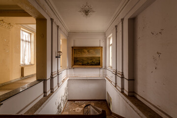 Abandoned elegant staircase with peeling walls and classic painting in a decaying historic building...