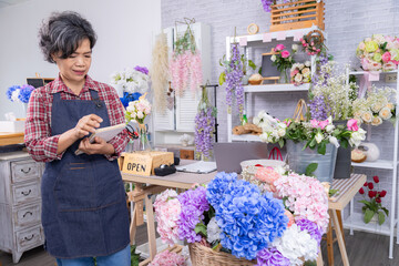 Small business lifestyle, flower working shop, Asian florist woman reviewing tablet orders, silver-haired female in retirement managing independent business in vibrant workplace, entrepreneurship
