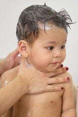 1 year old baby being bathed by mother, soap, water running over body, minimalist background with...