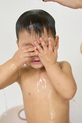 1 year old baby being bathed by mother, soap, water running over body, minimalist background with...