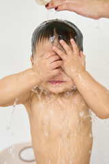 1 year old baby being bathed by mother, soap, water running over body, minimalist background with...