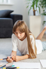 Girl lying on floor drawing with markers. Preparing for school.