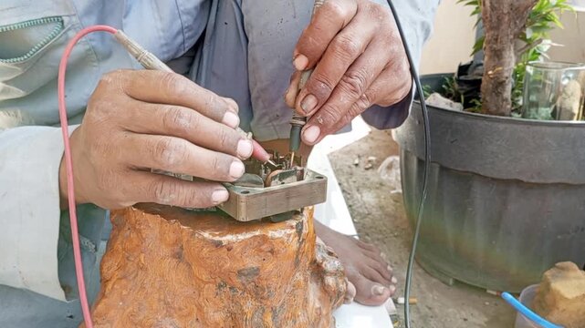 A broken dynamo may be repairable. A repairman carefully inspects the damaged dynamo's copper coil with an avometer to save on repair costs.