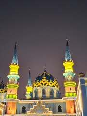 Colorful mosque illuminated at night, showcasing intricate architecture, vibrant minarets, and a patterned dome.