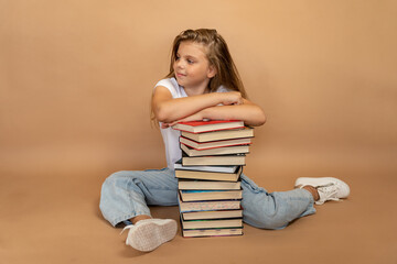 Education and school concept. Schoolgirl sitting leaning on a pile of books and looking aside on a...