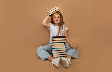 Education and school concept. Cheerful schoolgirl sitting next to a pile of books and putting books...