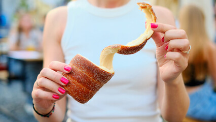 Close-up of a woman holding a freshly baked traditional trdelnik pastry with cinnamon coating,...