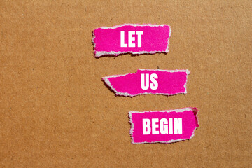 Let us begin message written on ripped torn pink paper pieces on cardboard background. Conceptual let us begin symbol. Copy space.