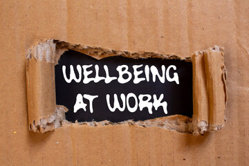 Wellbeing at work message written on ripped torn cardboard paper on black background. Conceptual...
