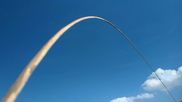 A blue kite with yellow tails soaring in the clear blue sky on a sunny day, accompanied by fluffy white clouds.
