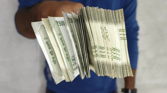 India rupee currency or indian money closeup. Young asian person hand offering stack of banknotes towards camera. pay, spend, tax, giving, deal, bribery, bribe, emi, corruption and success concept.