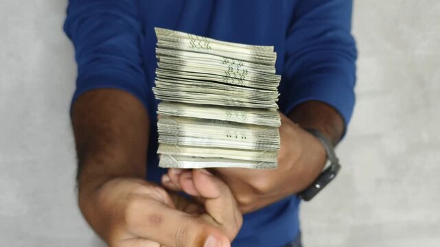 Close up of hand holding showing and flipping stack of 500 rupees Indian currency notes. Budget, savings, black money, profit, illegal income, wealth, success, corruption and bribery concept.