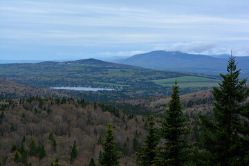 A wide, scenic view of a vast, forested valley with a lake nestled among the trees, under a cloudy sky, Québec, Canada