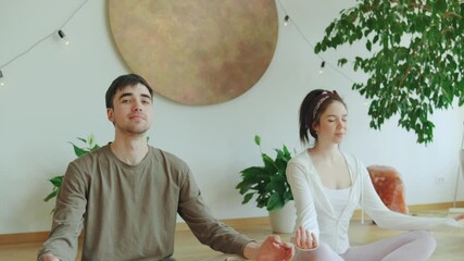 Meditation session for two individuals in a bright, serene indoor space surrounded by plants and soft lighting