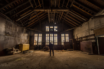 Photographer exploring an abandoned industrial building with large windows and rustic wooden roof...