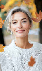 Beautiful 40-year-old woman in white knitted sweater with yellow autumn leaves