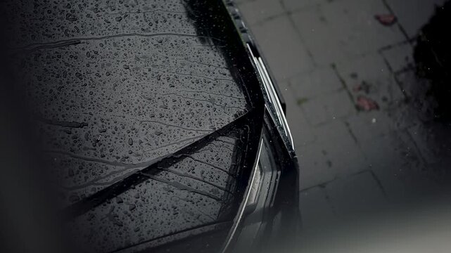 Rain drops slowly fall on the hood of a car prepared with a ceramic coating. Slow motion