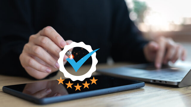 Hand holding stylus pointing at five-star checkmark icon on tablet. Concept for quality assurance, trusted service, customer rating, and verified review system.