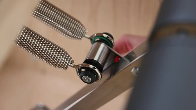 Hand adjusts spring on mechanical system of fitness machine or furniture in closeup view