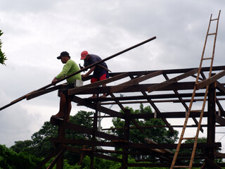 Silhouettes of carpenters on top of the wooden frame are joining girders and beams to construct a...