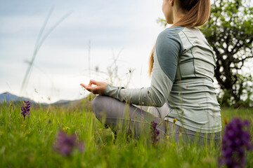 Cropped back view of a woman meditating in nature, peaceful female in sportswear sitting on green...