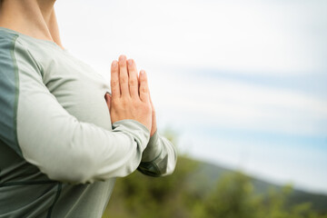 Close-up of young woman practicing meditation in nature at daylight, female hands in namaste gesture outdoors, wellness, mindfulness, zen energy concept