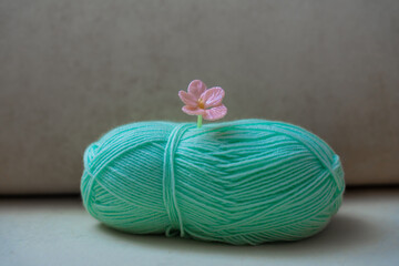 Close-up of pastel mint green yarn ball decorated with handcrafted pink glass flower pin. Soft...